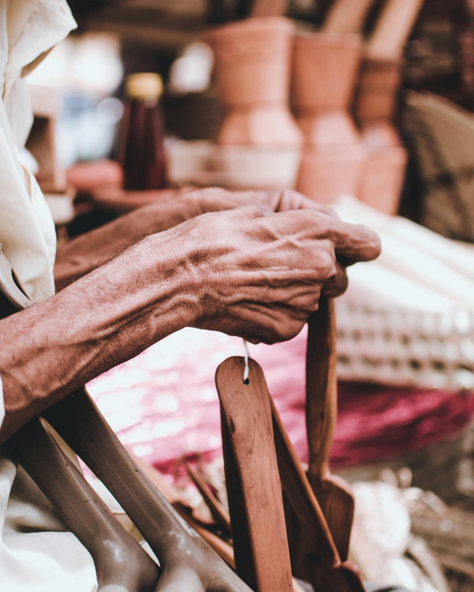 Close-up of an elderly artisan's hands skillfully crafting a wooden tool at an outdoor market.